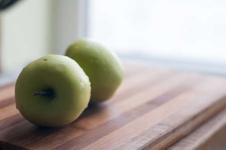 Two green apples lie on wooden cutting boardの写真素材