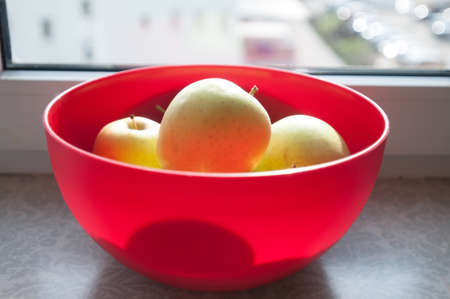 Green apples in red bowl sunny day on window sillの写真素材