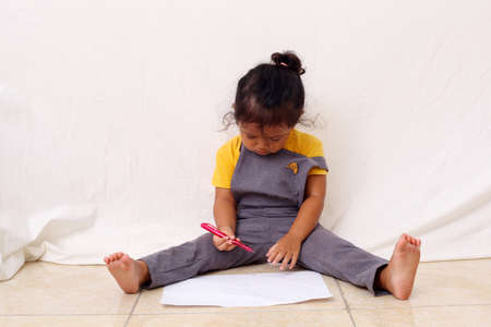 Adorable asian girl is sitting while learning to white. Isolated on white backgroundの写真素材