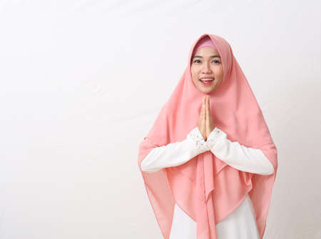 An Asian woman in Muslim dress stands up in a greetting pose to Namaste hands, welcoming guests, Ied...