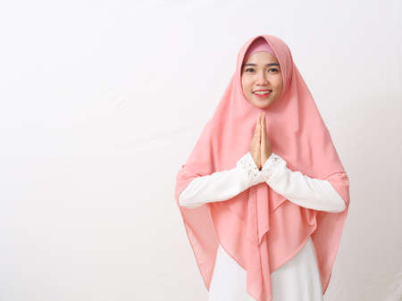 An Asian woman in Muslim dress stands up in a greetting pose to Namaste hands, welcoming guests, Ied Fitr greeting. Isolated on white backgroundの写真素材