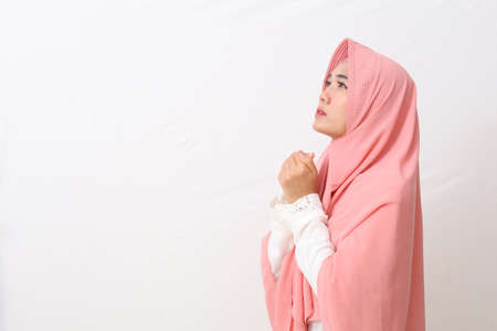 A portrait of asian muslim woman wearing a veil or hijab looking up and praying with closed hands gesture. Isolated on white background with copy spaceの写真素材