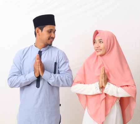 Portrait of asian muslim couple are doing a greeting pose as a symbol of forgiveness while looking each other. Asian Muslims are celebrating Eid Mubarak. Isolated on white background.の写真素材