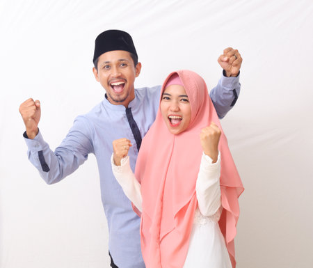 A portrait of a happy Muslim couple clenched fists. They feel successful. Isolated on white background.の写真素材