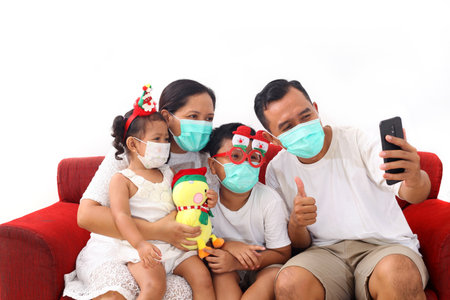 Asian happy family wearing masks is on a video call. The concept of celebrating Christmas during a...