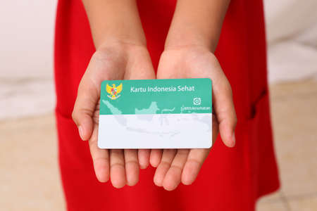 Yogyakarta, Indonesia - Dec 18, 2020 : Adorable Asian girl holds "Kartu Indonesia Sehat (KIS)" or card for health insurance for Indonesian residentsのeditorial素材