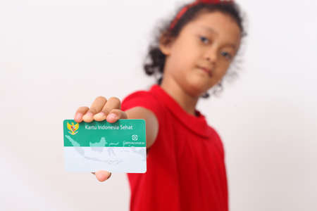 Yogyakarta, Indonesia - Dec 18, 2020 : Adorable Asian girl holds "Kartu Indonesia Sehat (KIS)" or card for health insurance for Indonesian residentsのeditorial素材