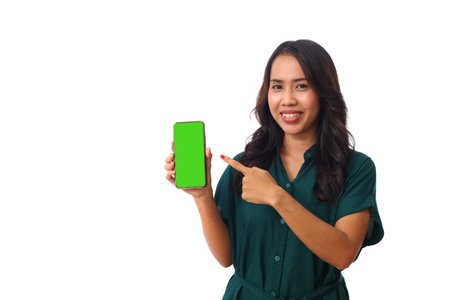 Portrait of Asian woman showing or presenting mobile cell phone with green screen and pointing finger to smartphone on hand isolated over white background.の写真素材