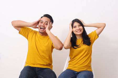 Cheerful asian couple sat with hands holding their heads with a happy expression. Isolated on white background with copyspaceの写真素材