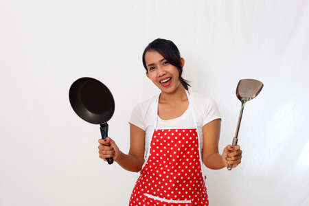 Portrait of happy asian woman wearing kitchen apron isolated on white background while carrying cooking wareの写真素材