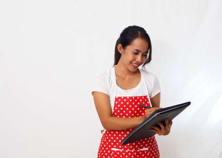 Portrait of asian woman wearing kitchen apron while writing on a food menu. Isolated on white backgroundの写真素材