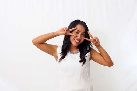 Young asian woman doing peace symbol with fingers over face, smiling cheerful showing victory