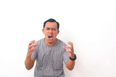 Asian man shouting frustrated with rage, hands trying to strangle, yelling mad. Isolated on white background with copyspaceの写真素材