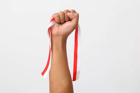 The hands of a man holding a red and white ribbon as a symbol of the Indonesian flag. Isolated on...