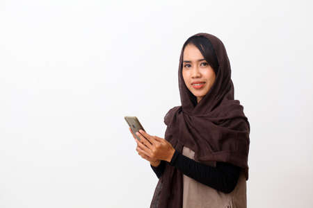 Portrait of happy asian muslim woman wearing a veil or hijab using a cell phone and smiling. Receiving good news, modern communication concept. Isolated on white background with copy spaceの写真素材