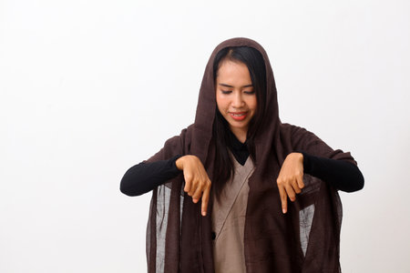 A portrait of happy asian muslim woman wearing a veil or hijab pointing or presenting something on empty space. Isolated on white background with copy spaceの写真素材
