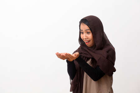 A portrait of happy asian muslim woman wearing a veil or hijab poiting or presenting something....