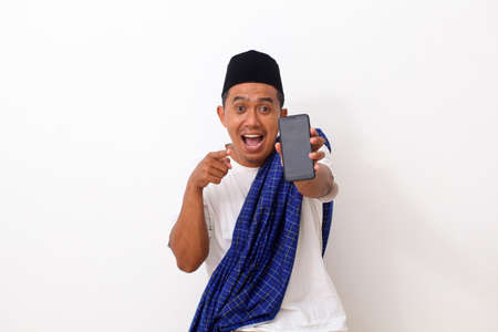 Portrait of happy asian man while standing and holding and pointing on phone cellular. Isolated on white. Ramadan conceptの写真素材