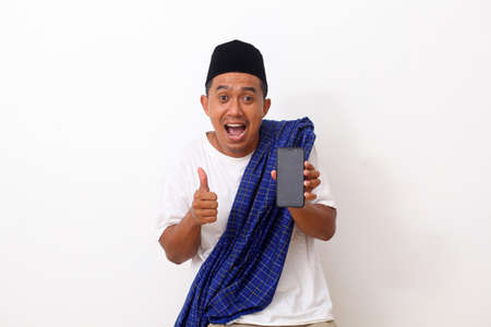 Portrait of happy asian man while standing and holding a phone cellular. Isolated on white. Ramadan conceptの写真素材