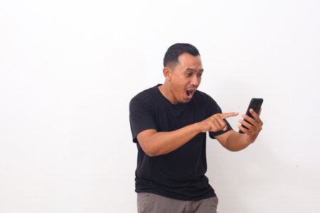 Wow and shocked face of Asian man while looking and pointing at his cellular phone. Isolated on...