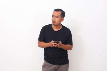 Asian Man feels hate and disgusted with what show on the smartphone while looking sideways. Isolated on white backgroundの写真素材