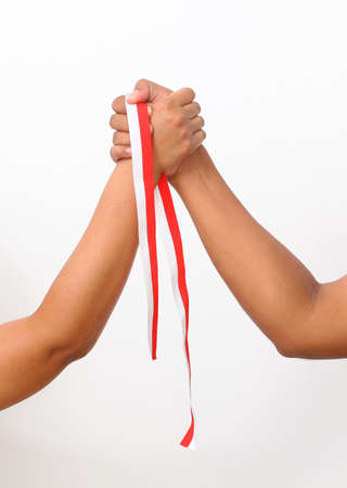 The hands of humans holding a red and white ribbon as a symbol of the Indonesian flag. Isolated on white backgroundの写真素材