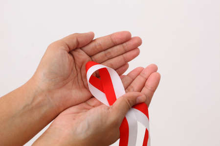 A human hand holds red white ribbon as symbol of the Indonesian flag. Isolated on white backgroundの写真素材