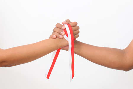 The hands of humans holding a red and white ribbon as a symbol of the Indonesian flag. Isolated on white backgroundの写真素材