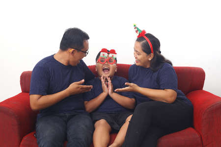 Asian family celebrating Christmas and New Year while sitting on red sofa. Isolated on white backgroundの写真素材