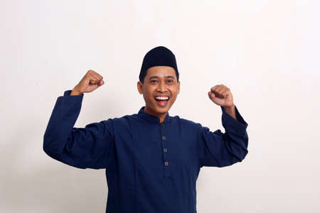 Happy winner. Happy asian man gesturing while standing against white backgroundの写真素材