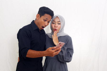 Amazed asian muslim couple standing while getting news from their cellular phone.の写真素材