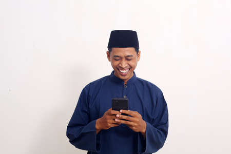 Happy asian muslim man while looking cellular phone.の写真素材