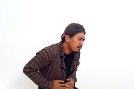 Asian man in java traditional costume having stomachache on white background, health concept.