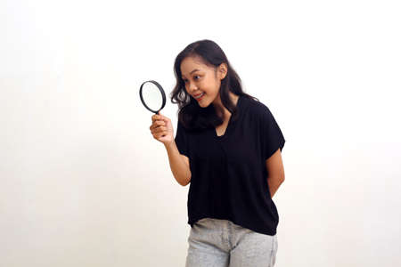 Asian young woman standing while looking through magnifying glass. Isolated on whiteの写真素材