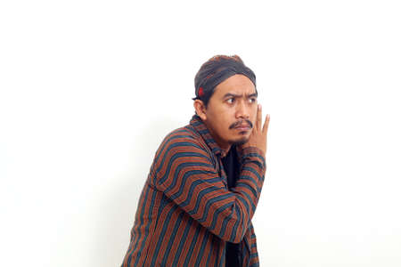 Curious asian man standing while looking sideways and trying to listening something.