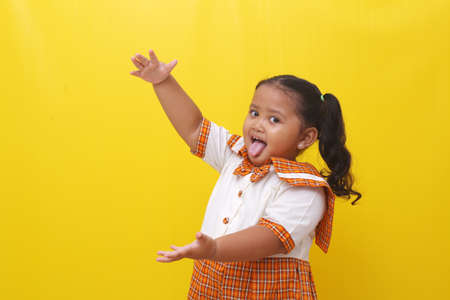 Asian little schoolgirl standing while presenting something. Isolated on yellow background