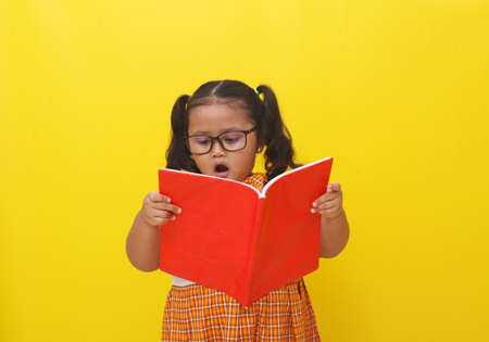 Cute Asian little schoolgirl standing while reading a book. Back to school concept.の写真素材
