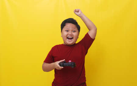 Winning asian boy standing while holding a joystick. Gaming concept. Isolated on yellow backgroundの写真素材