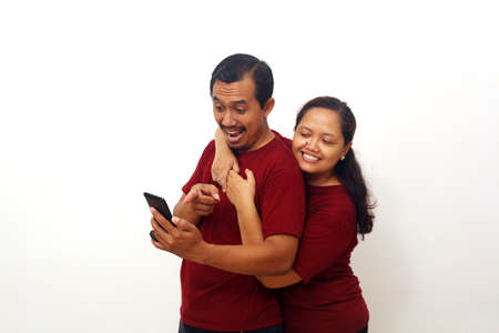 Surprised Asian couple standing while holding a cellular phone. Isolated on white background