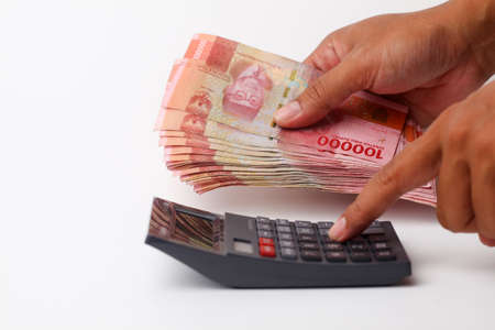 Hand using calculator while holding banknotes. Isolated on white background with copyspace