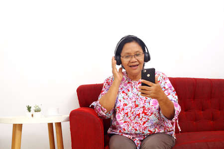 Excited elderly asian woman doing video call using headphone at home, isolated with copyspaceの写真素材