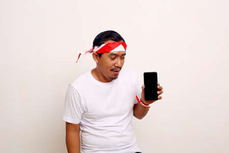 Asian man standing while presenting blank cell phone screen with indonesian independence day conceptの写真素材