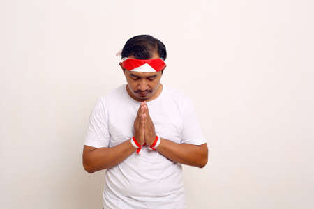 Asian man standing with praying gesture for celebrating indonesian independence day.