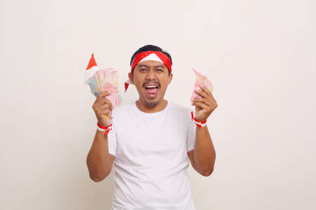 Happy asian man standing while holding indonesian money. Celebrating Independence day conceptの写真素材
