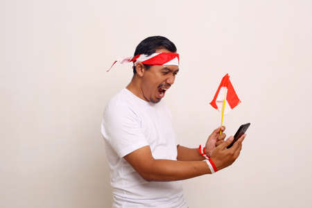 Excited Indonesian man standing while getting good news from his cell phone.Independence day conceptの写真素材
