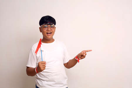 Asian boy holding indonesian flag while pointing sideways. Isolated on white with copyspaceの写真素材