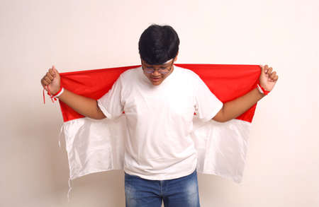 Happy asian boy standing while carrying indonesian flag and looking down. Independence day conceptの写真素材