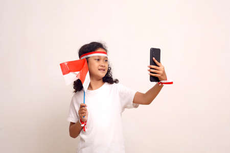 Asian girl doing selfie while holding indonesian flag. Isolated on white with copyspace