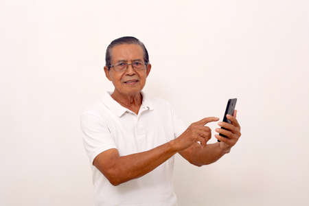 Happy asian old man standing while pointing or using a cell phone. Isolated on white