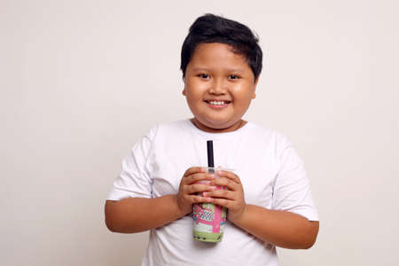 Happy asian boy standing while holding a drinking package. Isolated on white